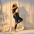 Woman wearing Gaia Luxury Women's Faux Leather High-Waisted Black Leggings, posing in a chic yoga position, showcasing designer athleisure wear
